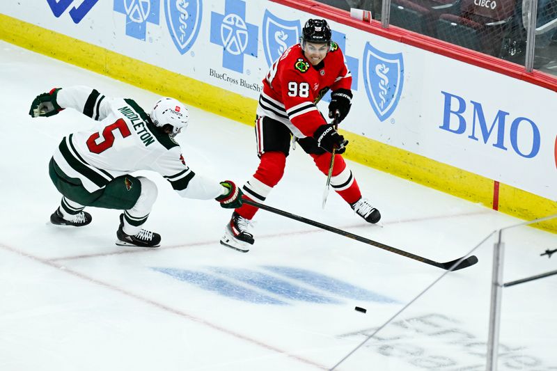 Nov 10, 2024; Chicago, Illinois, USA;  Minnesota Wild defenseman Jake Middleton (5) and Chicago Blackhawks center Connor Bedard (98) chase the puck during the second period at the United Center. Mandatory Credit: Matt Marton-Imagn Images