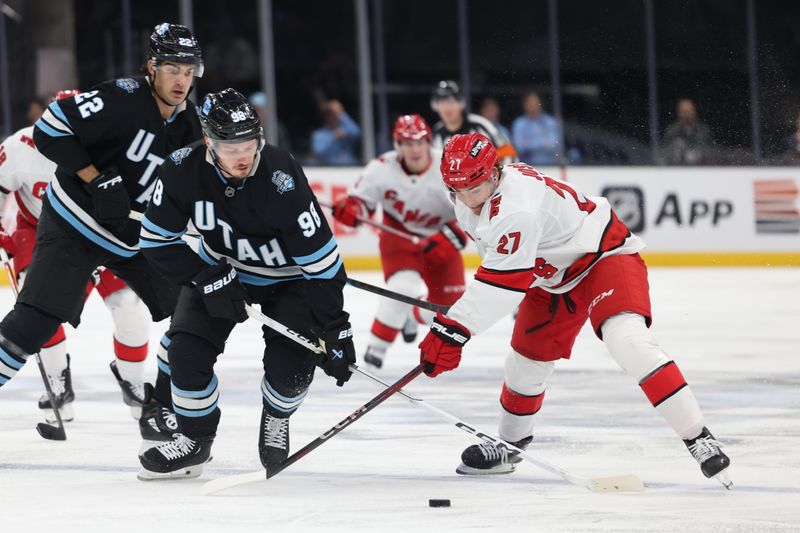 Nov 13, 2024; Salt Lake City, Utah, USA; Utah Hockey Club defenseman Mikhail Sergachev (98) and Carolina Hurricanes center Tyson Jost (27) play the puck during the second period at Delta Center. Mandatory Credit: Rob Gray-Imagn Images