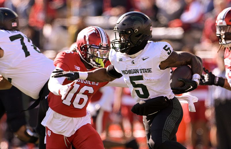 Nov 18, 2023; Bloomington, Indiana, USA; Michigan State Spartans running back Nathan Carter (5) runs the ball under pressure from Indiana Hoosiers defensive back Jordan Grier (16) during the first half at Memorial Stadium. Mandatory Credit: Marc Lebryk-USA TODAY Sports