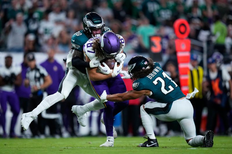 Minnesota Vikings tight end T.J. Hockenson (87) is stopped by Philadelphia Eagles safety Justin Evans (30) and Philadelphia Eagles safety Sydney Brown (21) during the first half of an NFL football game Thursday, Sept. 14, 2023, in Philadelphia. (AP Photo/Matt Slocum)