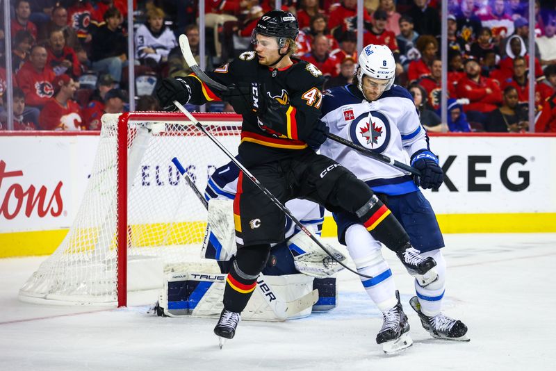 Oct 26, 2024; Calgary, Alberta, CAN; Calgary Flames center Connor Zary (47) and Winnipeg Jets defenseman Colin Miller (6) fights for position in front of Winnipeg Jets goaltender Eric Comrie (1) during the second period at Scotiabank Saddledome. Mandatory Credit: Sergei Belski-Imagn Images