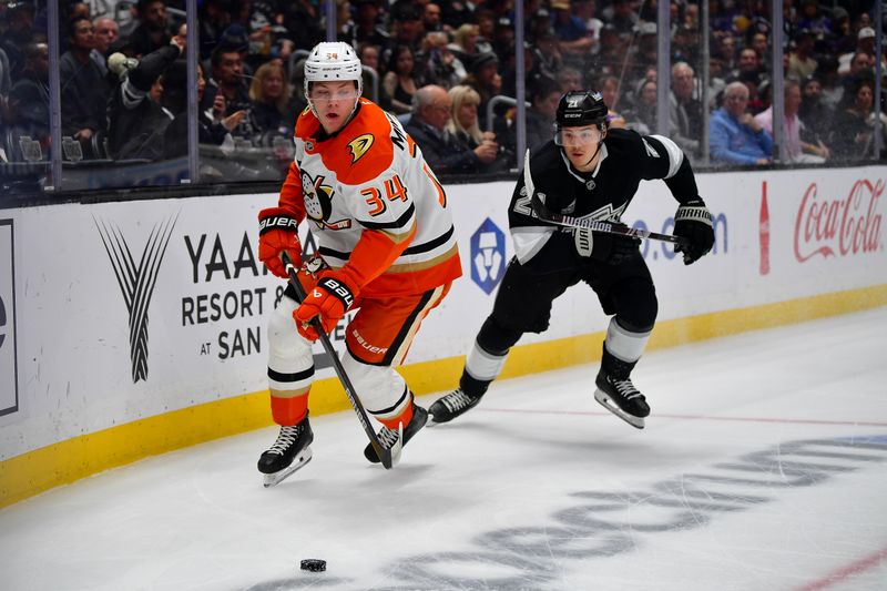 Apr 10, 2025; Los Angeles, California, USA; Anaheim Ducks defenseman Pavel Mintyukov (34) moves the puck ahead of Los Angeles Kings defenseman Jordan Spence (21) during the first period at Crypto.com Arena. Mandatory Credit: Gary A. Vasquez-Imagn Images