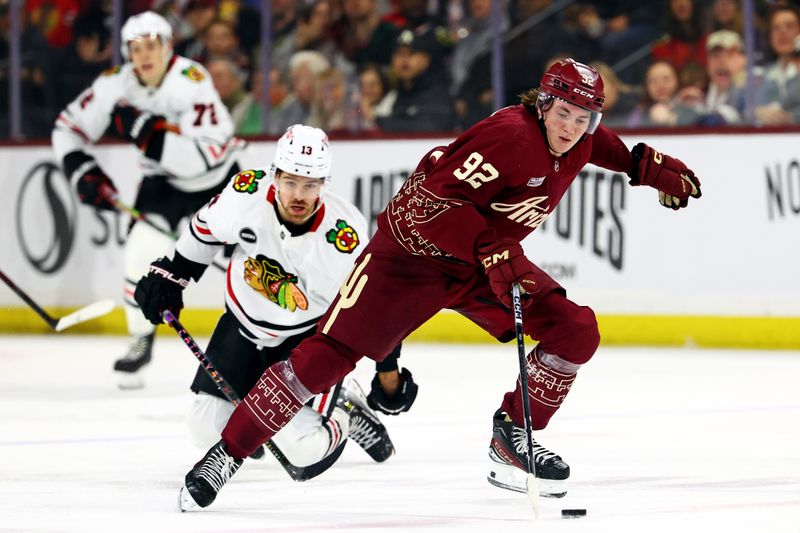 Mar 5, 2024; Tempe, Arizona, USA;  Arizona Coyotes center Logan Cooley (92) moves the puck against Chicago Blackhawks left wing Zach Sanford (13) during the second period at Mullett Arena. Mandatory Credit: Mark J. Rebilas-USA TODAY Sports