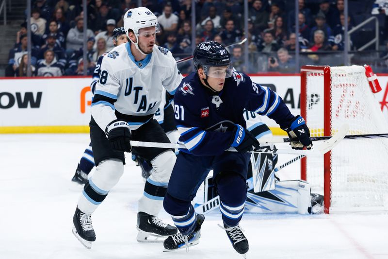 Nov 5, 2024; Winnipeg, Manitoba, CAN;  Winnipeg Jets forward Cole Perfetti (91) and Utah Hockey Club defenseman Mikhail Sergachev (98) look for the puck during the second period at Canada Life Centre. Mandatory Credit: Terrence Lee-Imagn Images