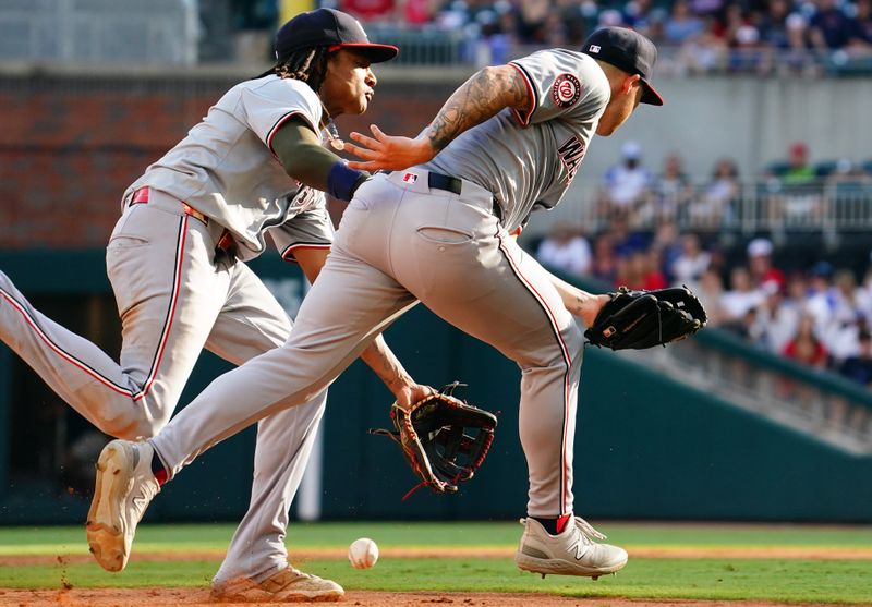 May 27, 2024; Cumberland, Georgia, USA; Atlanta Braves catcher Sean Murphy (12) hits an infield single on an error as Washington Nationals shortstop CJ Abrams (5) and Washington Nationals third baseman Nick Senzel (13) bobble the ball during the ninth inning at Truist Park. Mandatory Credit: John David Mercer-USA TODAY Sports