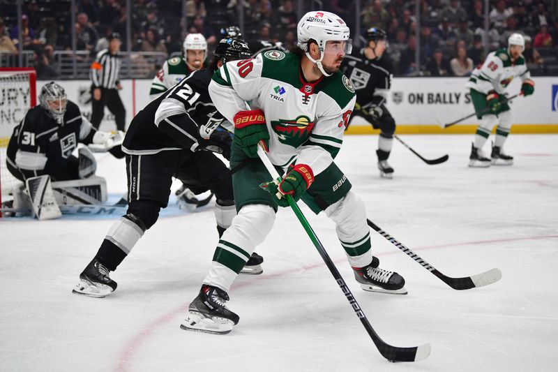 Mar 20, 2024; Los Angeles, California, USA; Minnesota Wild center Marcus Johansson (90) moves the puck ahead of Los Angeles Kings defenseman Jordan Spence (21)  during the first period at Crypto.com Arena. Mandatory Credit: Gary A. Vasquez-USA TODAY Sports