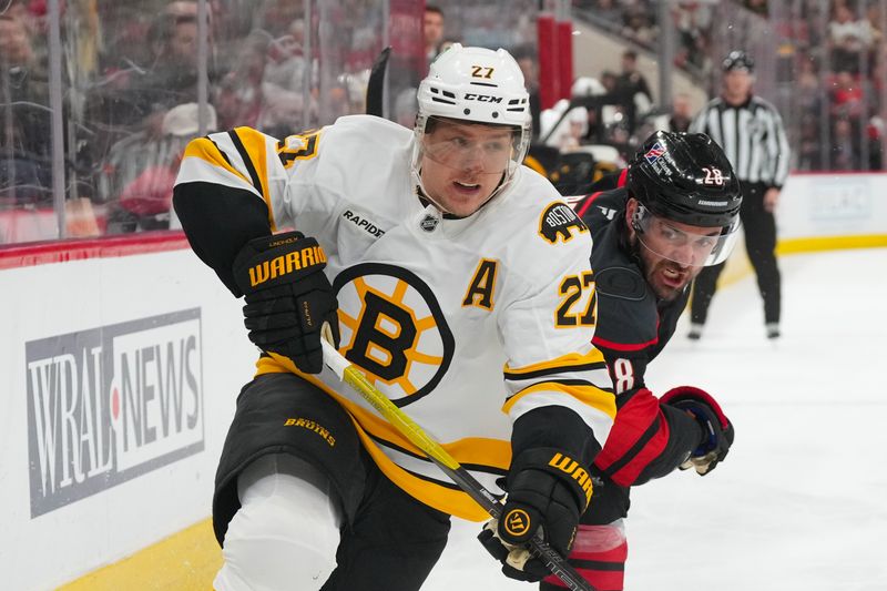 Apr 7, 2026; Raleigh, North Carolina, USA;  Boston Bruins defenseman Hampus Lindholm (27) and Carolina Hurricanes left wing William Carrier (28) battle during the second period at Lenovo Center. Mandatory Credit: James Guillory-Imagn Images