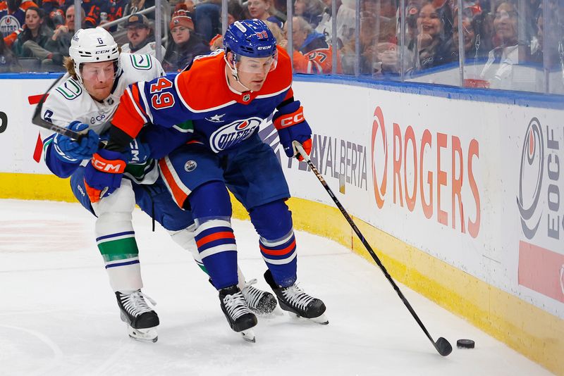 Jan 23, 2025; Edmonton, Alberta, CAN; Edmonton Oilers defensemen Ty Emberson (49) protects the puck from Vancouver Canucks forward Brock Boeser (6) during the second period at Rogers Place. Mandatory Credit: Perry Nelson-Imagn Images