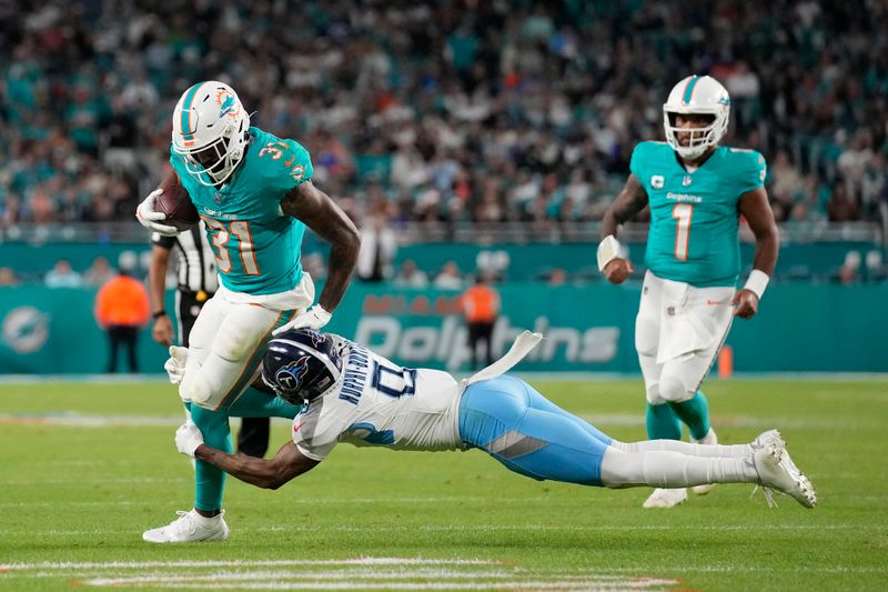 Tennessee Titans cornerback Sean Murphy-Bunting (0) grabs Miami Dolphins running back Raheem Mostert (31) during the second half of an NFL football game, Monday, Dec. 11, 2023, in Miami. (AP Photo/Rebecca Blackwell)