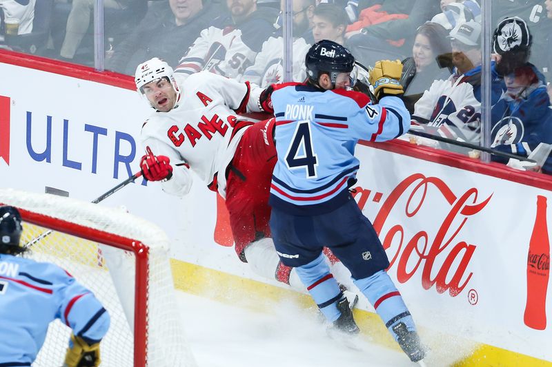 Dec 4, 2023; Winnipeg, Manitoba, CAN; Winnipeg Jets defenseman Neal Pionk (4) boards Carolina Hurricanes forward Jordan Martinook (48) during the third period at Canada Life Centre. Mandatory Credit: Terrence Lee-USA TODAY Sports