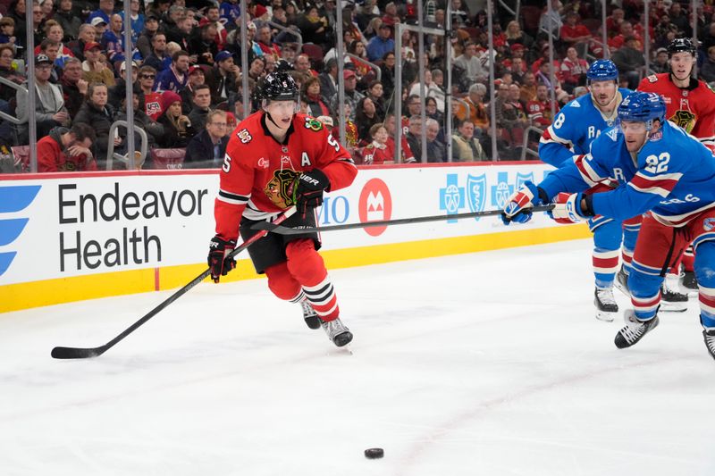 Dec 10, 2025; Chicago, Illinois, USA; New York Rangers center Jonny Brodzinski (22) and Chicago Blackhawks defenseman Connor Murphy (5) go for the puck during the third period at United Center. Mandatory Credit: David Banks-Imagn Images
