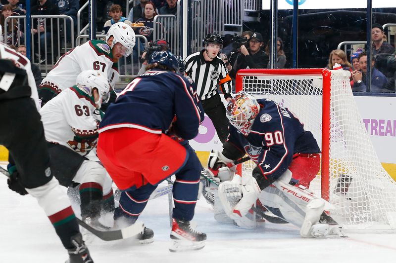 Nov 16, 2023; Columbus, Ohio, USA; Columbus Blue Jackets goalie Elvis Merzlikins (90) makes a save as Arizona Coyotes left wing Matias Maccelli (63) and left wing Lawson Crouse (67) look for a rebound during the first period at Nationwide Arena. Mandatory Credit: Russell LaBounty-USA TODAY Sports