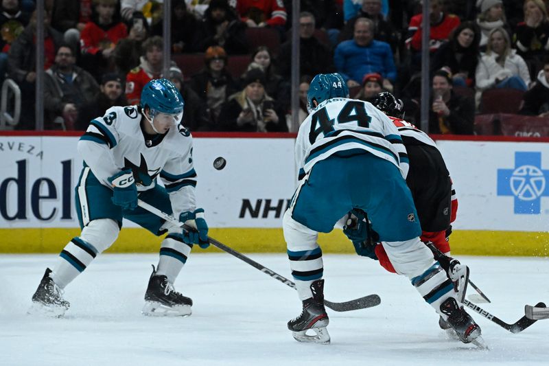 Jan 16, 2024; Chicago, Illinois, USA; Chicago Blackhawks center Cole Guttman (70) moves the puck against San Jose Sharks defenseman Henry Thrun (3) and San Jose Sharks defenseman Marc-Edouard Vlasic (44) during the first period at United Center. Mandatory Credit: Matt Marton-USA TODAY Sports