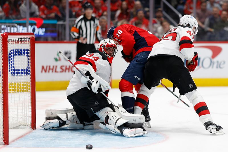 Nov 23, 2024; Washington, District of Columbia, USA; New Jersey Devils goaltender Jake Allen (34) makes a save on Washington Capitals right wing Taylor Raddysh (16) as Devils defenseman Luke Hughes (43) defends in the third period at Capital One Arena. Mandatory Credit: Geoff Burke-Imagn Images