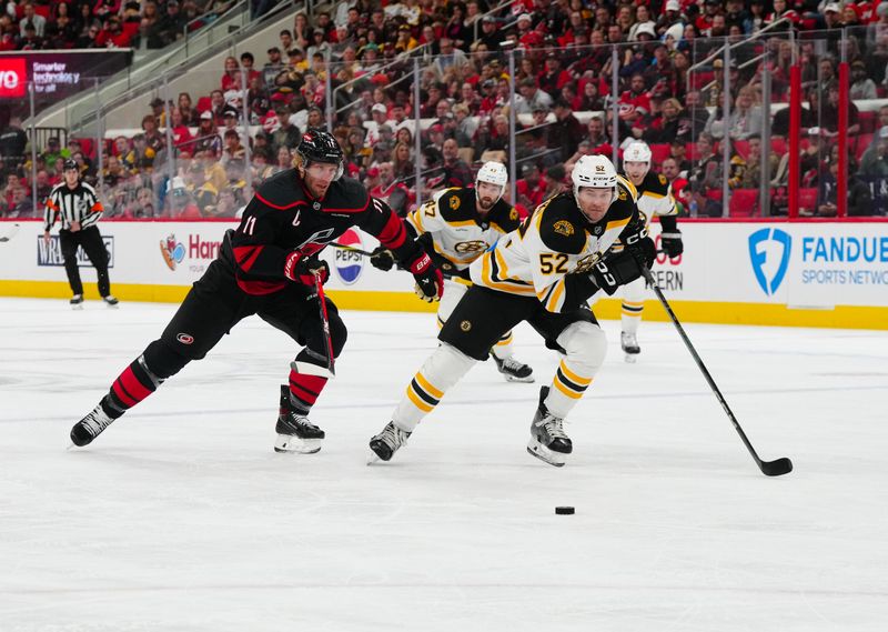 Oct 31, 2024; Raleigh, North Carolina, USA;  Carolina Hurricanes center Jordan Staal (11) and Boston Bruins defenseman Andrew Peeke (52) skate after the puck during the first period at Lenovo Center. Mandatory Credit: James Guillory-Imagn Images