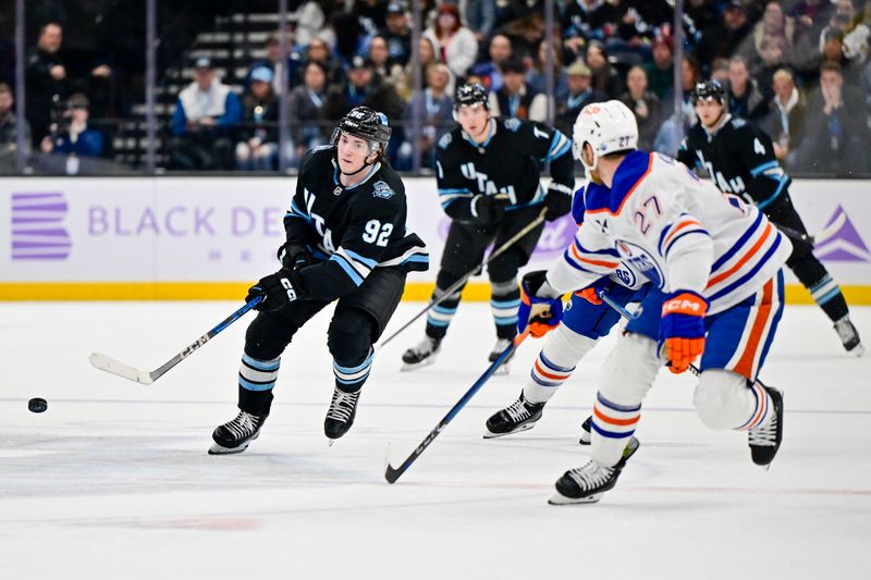 Nov 29, 2024; Salt Lake City, Utah, USA; Utah Hockey Club center Logan Cooley (92) passes the puck past Edmonton Oilers defenseman Brett Kulak (27) during the second period at the Delta Center. Mandatory Credit: Christopher Creveling-Imagn Images