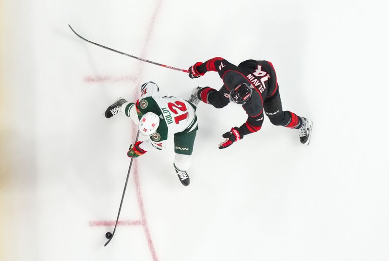 Jan 21, 2024; Raleigh, North Carolina, USA;  Minnesota Wild left wing Matt Boldy (12) skates with the puck against Carolina Hurricanes defenseman Jaccob Slavin (74) during the second period at PNC Arena. Mandatory Credit: James Guillory-USA TODAY Sports