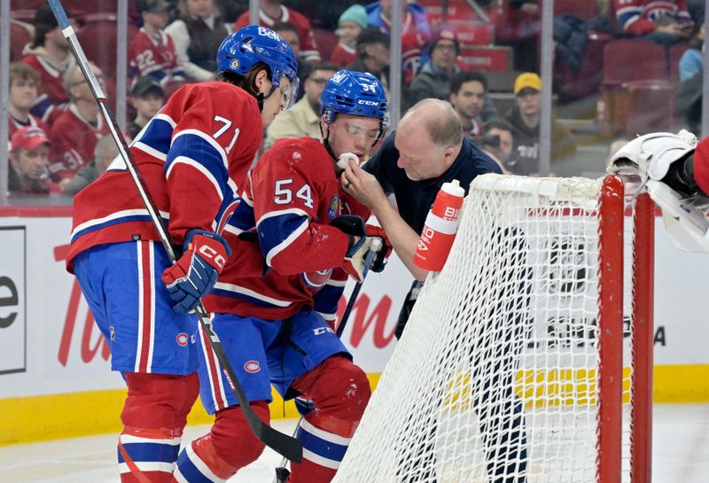 Feb 11, 2024; Montreal, Quebec, CAN; Montreal Canadiens trainer and Montreal Canadiens forward Jake Evans (71) tend to injured teammate defenseman Jordan Harris (54) after he was hit by a St.Louis Blues player during the first period at the Bell Centre. Mandatory Credit: Eric Bolte-USA TODAY Sports