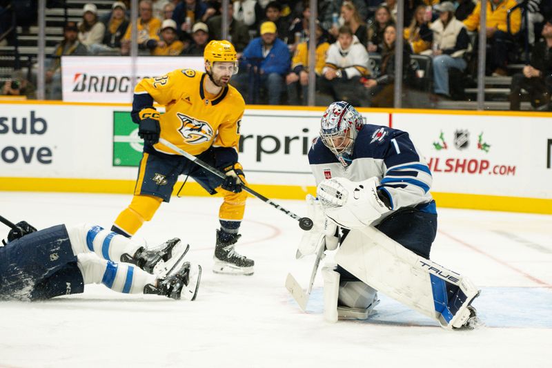 Nov 23, 2024; Nashville, Tennessee, USA;  Winnipeg Jets goaltender Eric Comrie (1) blocks the shot from Nashville Predators center Tommy Novak (82) during the third period at Bridgestone Arena. Mandatory Credit: Steve Roberts-Imagn Images