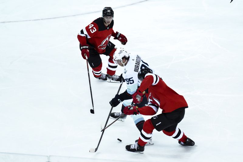 Feb 12, 2024; Newark, New Jersey, USA; Seattle Kraken left wing Andre Burakovsky (95) skates with the puck while being defended by New Jersey Devils defenseman Luke Hughes (43) and defenseman John Marino (6) during the third period at Prudential Center. Mandatory Credit: John Jones-USA TODAY Sports