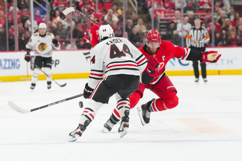 Jan 22, 2026; Raleigh, North Carolina, USA;  Carolina Hurricanes center Jordan Staal (11) chips the puck past Chicago Blackhawks defenseman Wyatt Kaiser (44) during the first period at Lenovo Center. Mandatory Credit: James Guillory-Imagn Images