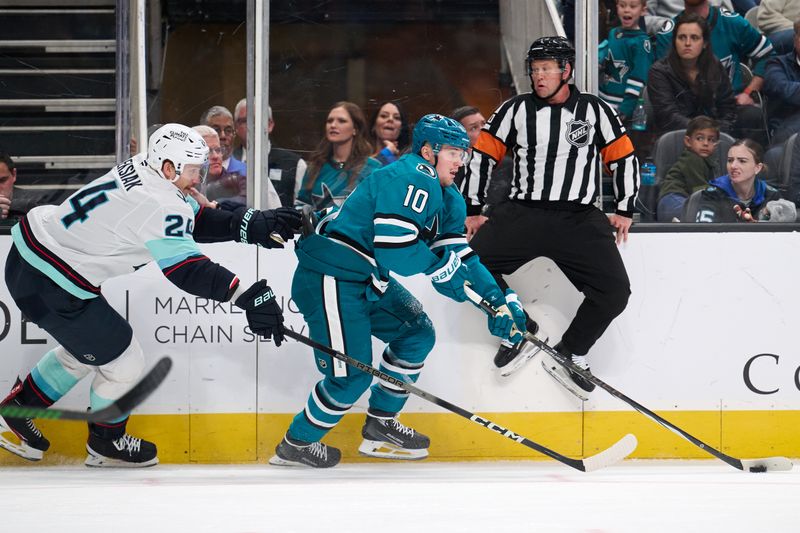 Nov 29, 2024; San Jose, California, USA; San Jose Sharks center Klim Kostin (10) plays the puck against Seattle Kraken defenseman Jamie Oleksiak (24) as referee Kyle Rehman (10) watches the play during the second period at SAP Center at San Jose. Mandatory Credit: Robert Edwards-Imagn Images