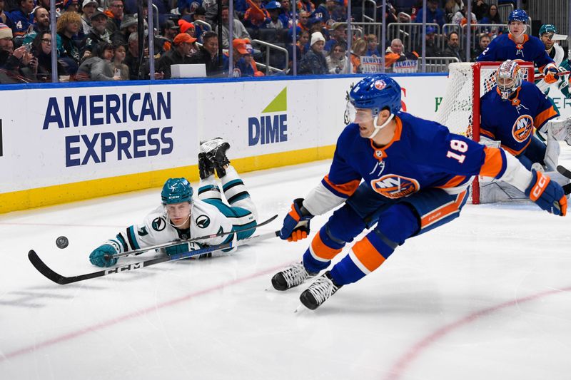 Dec 5, 2023; Elmont, New York, USA; San Jose Sharks center Nico Sturm (7) dives for a loose puck defended by New York Islanders left wing Pierre Engvall (18) during the first period at UBS Arena. Mandatory Credit: Dennis Schneidler-USA TODAY Sports