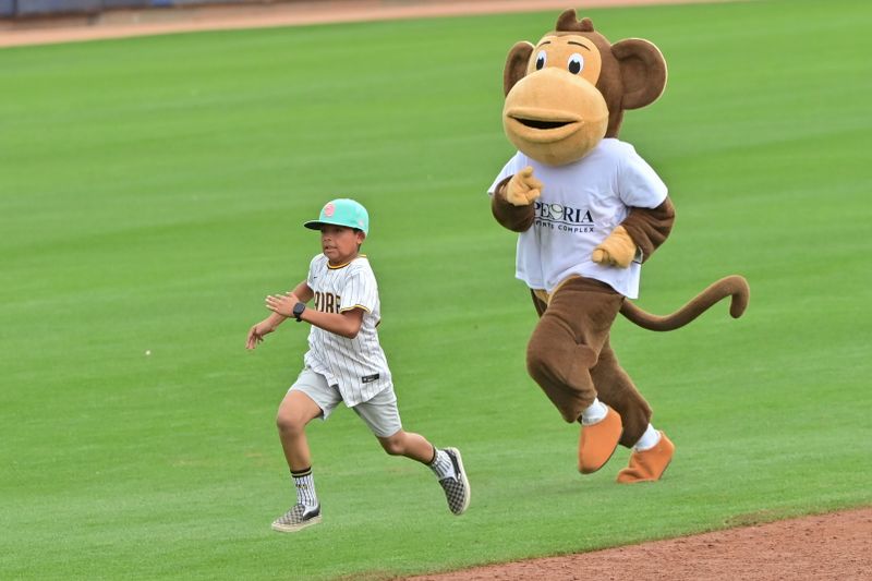 Feb 26, 2024; Peoria, Arizona, USA;  A monkey mascot chases a young San Diego Padres fan in the third inning against the Cleveland Guardians during a spring training game at Peoria Sports Complex. Mandatory Credit: Matt Kartozian-USA TODAY Sports