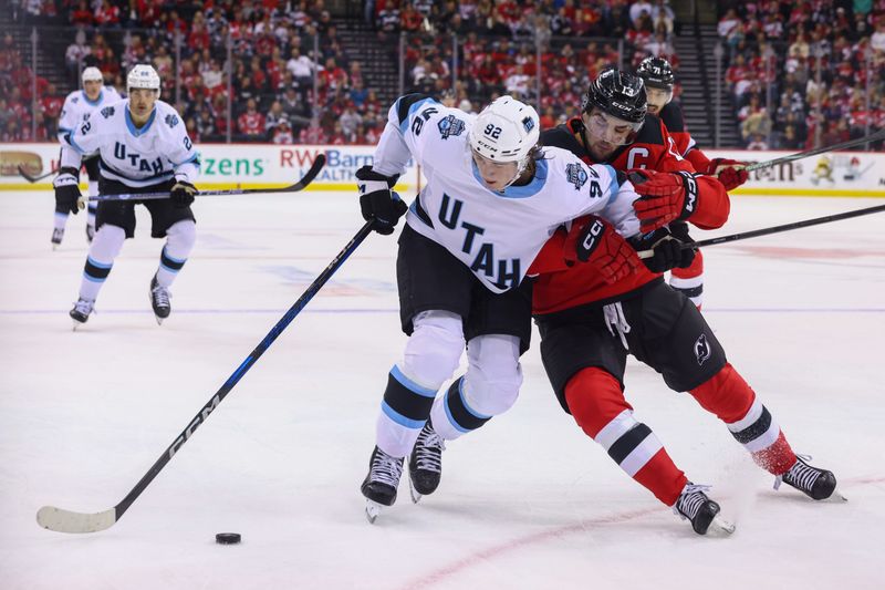 Oct 14, 2024; Newark, New Jersey, USA; Utah Hockey Club center Logan Cooley (92) and New Jersey Devils center Nico Hischier (13) battle for the puck during the first period at Prudential Center. Mandatory Credit: Ed Mulholland-Imagn Images