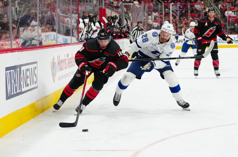 Oct 11, 2024; Raleigh, North Carolina, USA;  Carolina Hurricanes center Jack Drury (18) and Tampa Bay Lightning center Zemgus Girgensons (28) chase after the puck during the second period at PNC Arena. Mandatory Credit: James Guillory-Imagn Images