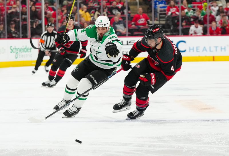 Nov 25, 2024; Raleigh, North Carolina, USA;  Dallas Stars left wing Jamie Benn (14) and Carolina Hurricanes defenseman Shayne Gostisbehere (4) chase after the puck during the second period at Lenovo Center. Mandatory Credit: James Guillory-Imagn Images