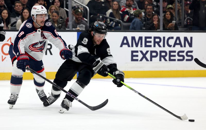 Nov 9, 2024; Los Angeles, California, USA; Los Angeles Kings right wing Adrian Kempe (9) keeps the puck from Columbus Blue Jackets defenseman Zach Werenski (8) during the second period at Crypto.com Arena. Mandatory Credit: Jason Parkhurst-Imagn Images