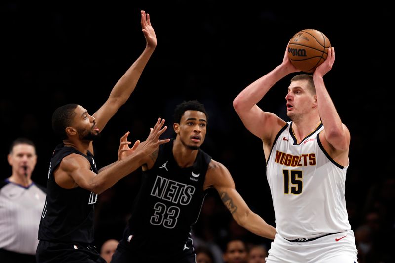 NEW YORK, NEW YORK - DECEMBER 22: Nikola Jokic #15 of the Denver Nuggets looks to pass as Mikal Bridges #1 and Nic Claxton #33 of the Brooklyn Nets defend during the first half at Barclays Center on December 22, 2023 in the Brooklyn borough of New York City. NOTE TO USER: User expressly acknowledges and agrees that, by downloading and/or using this Photograph, user is consenting to the terms and conditions of the Getty Images License Agreement. (Photo by Sarah Stier/Getty Images)