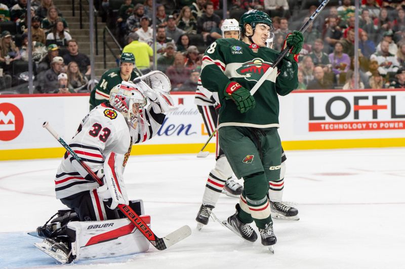 Oct 1, 2024; Saint Paul, Minnesota, USA; Chicago Blackhawks goaltender Drew Commesso (33) deflects a shot with his glove as Minnesota Wild left wing Liam Ohgren (28) moves to avoid the shot in the second period at Xcel Energy Center. Mandatory Credit: Matt Blewett-Imagn Images