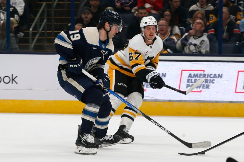 Nov 15, 2024; Columbus, Ohio, USA; Columbus Blue Jackets center Adam Fantilli (19) carries the puck as Pittsburgh Penguins center Rickard Rakell (67) defends during the first period at Nationwide Arena. Mandatory Credit: Russell LaBounty-Imagn Images
