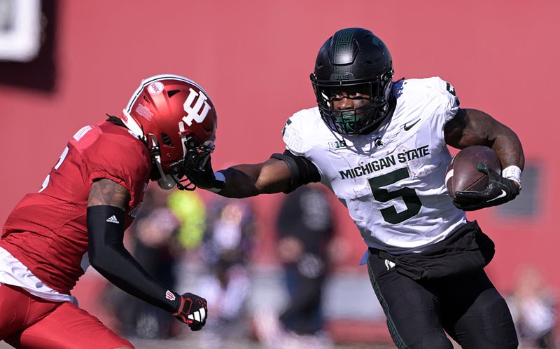 Nov 18, 2023; Bloomington, Indiana, USA; Michigan State Spartans running back Nathan Carter (5) stiff arms Indiana Hoosiers defensive back Phillip Dunnam (6) during the first quarter at Memorial Stadium. Mandatory Credit: Marc Lebryk-USA TODAY Sports