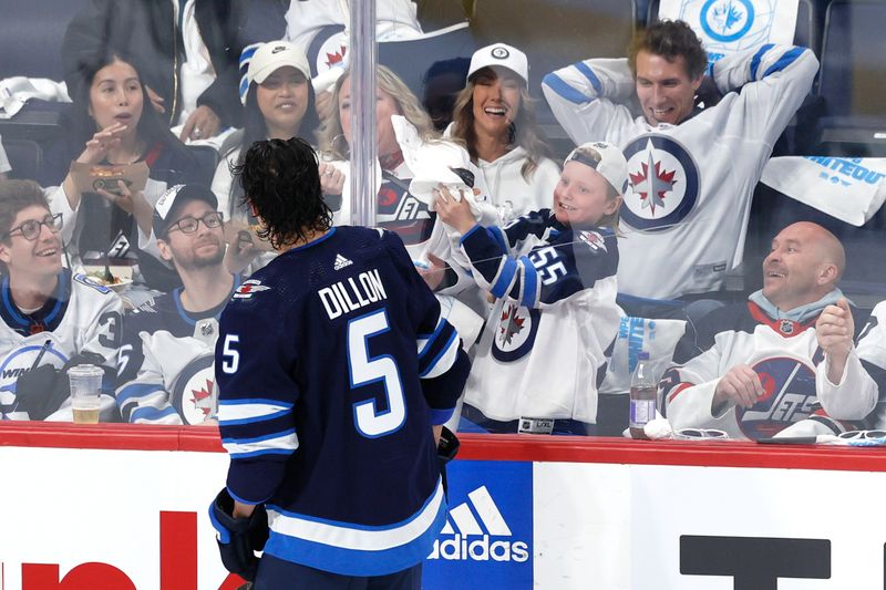 Apr 21, 2024; Winnipeg, Manitoba, CAN; Winnipeg Jets defenseman Brenden Dillon (5) tosses a puck to a fan before a game against the Colorado Avalanche in game one of the first round of the 2024 Stanley Cup Playoffs at Canada Life Centre. Mandatory Credit: James Carey Lauder-USA TODAY Sports