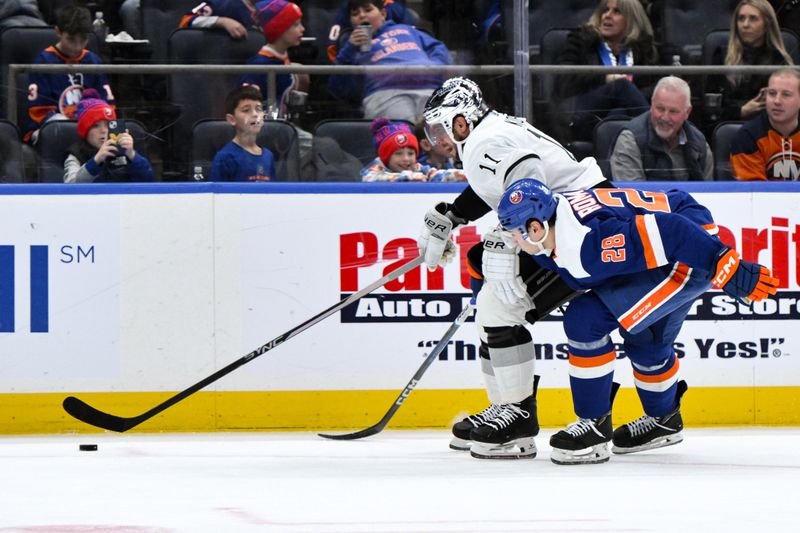 Dec 9, 2023; Elmont, New York, USA; Los Angeles Kings center Anze Kopitar (11) moves the puck past New York Islanders defenseman Alexander Romanov (28) during the first period at UBS Arena. Mandatory Credit: John Jones-USA TODAY Sports