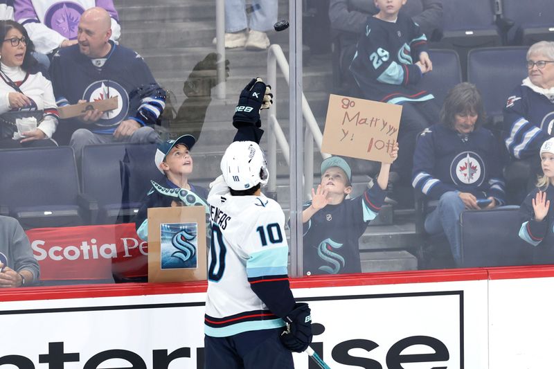 Oct 23, 2025; Winnipeg, Manitoba, CAN; Seattle Kraken center Matty Beniers (10) tosses a puck to a fan before a game against the Winnipeg Jets at Canada Life Centre. Mandatory Credit: James Carey Lauder-Imagn Images