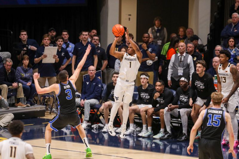 Feb 11, 2025; Morgantown, West Virginia, USA; West Virginia Mountaineers guard Joseph Yesufu (1) shoots a three pointer over Brigham Young Cougars guard Egor Demin (3) during the second half at WVU Coliseum. Mandatory Credit: Ben Queen-Imagn Images