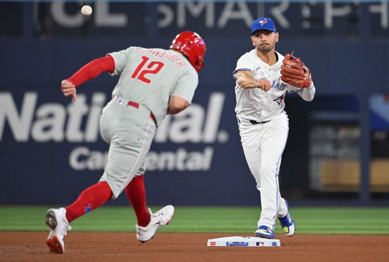 Jun 4, 2025; Toronto, Ontario, CAN;  Toronto Blue Jays second baseman Andres Gimenez (0) throws to first for a double play after forcing out Philadelphia Phillis designated hitter Kyle Schwarber (12) in the fourt inning at Rogers Centre. Mandatory Credit: Dan Hamilton-Imagn Images