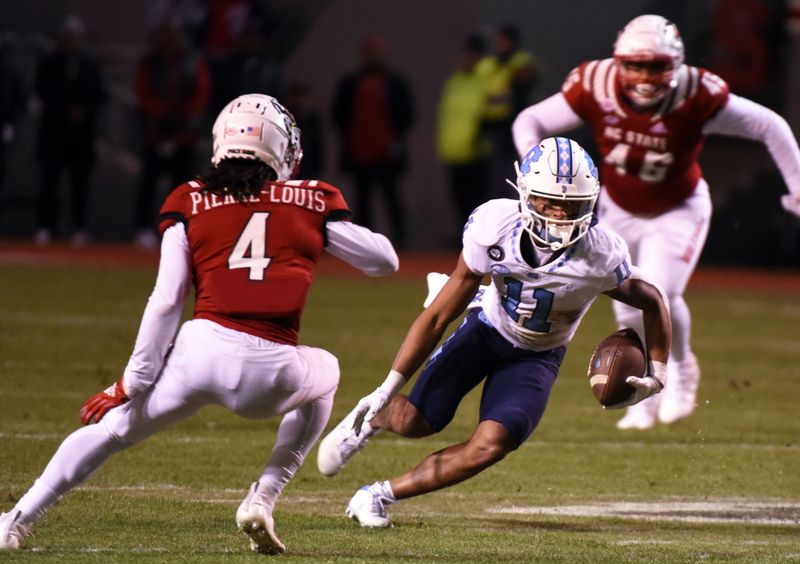 Nov 26, 2021; Raleigh, North Carolina, USA;  North Carolina Tar Heels wide receiver Josh Downs (11) runs after the catch as North Carolina State Wolfpack defensive back Joshua Pierre-Louis (4) defends during the first half at Carter-Finley Stadium. Mandatory Credit: Rob Kinnan-USA TODAY Sports