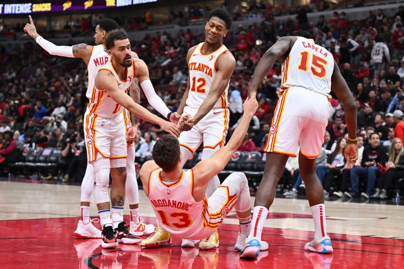 CHICAGO, ILLINOIS - APRIL 17:  Bogdan Bogdanovic #13 of the Atlanta Hawks is helped up by teammates Trae Young #11, De'Andre Hunter #12 and Clint Capela #15 after drawing a foul in the second half against the Chicago Bulls on April 17, 2024 at United Center in Chicago, Illinois. Chicago defeated Atlanta 131-116.   NOTE TO USER: User expressly acknowledges and agrees that, by downloading and or using this photograph, User is consenting to the terms and conditions of the Getty Images License Agreement.  (Photo by Jamie Sabau/Getty Images)