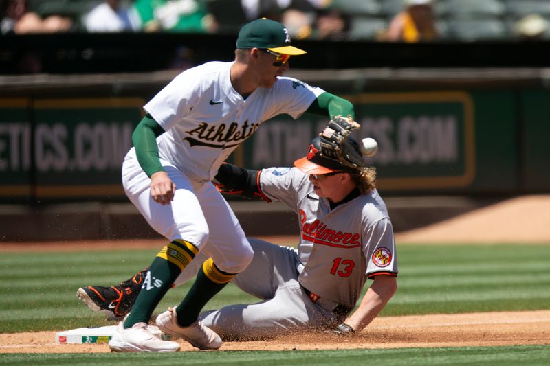 Jul 7, 2024; Oakland, California, USA; Baltimore Orioles left fielder Heston Kjerstad (13) slides safely into third ahead the relay to Oakland Athletics third baseman Brett Harris (77) on a fly ball to center that was scored a three-base error during the third inning at Oakland-Alameda County Coliseum. Mandatory Credit: D. Ross Cameron-USA TODAY Sports