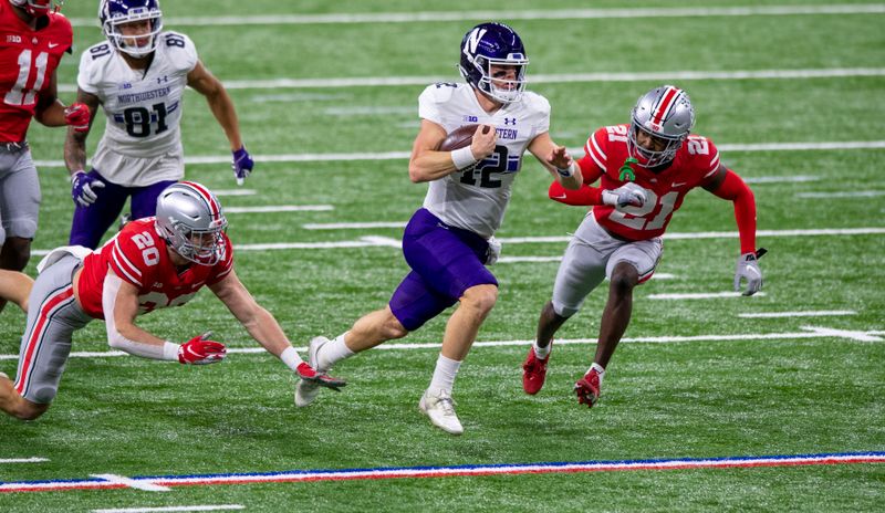 Dec 19, 2020; Indianapolis, Indiana, USA; Northwestern Wildcats quarterback Peyton Ramsey (12) runs the ball against Ohio State Buckeyes linebacker Pete Werner (20) and cornerback Marcus Williamson (21)  during the first half of the Big Ten Championship game at Lucas Oil Stadium. Mandatory Credit: Doug McSchooler-USA TODAY Sports