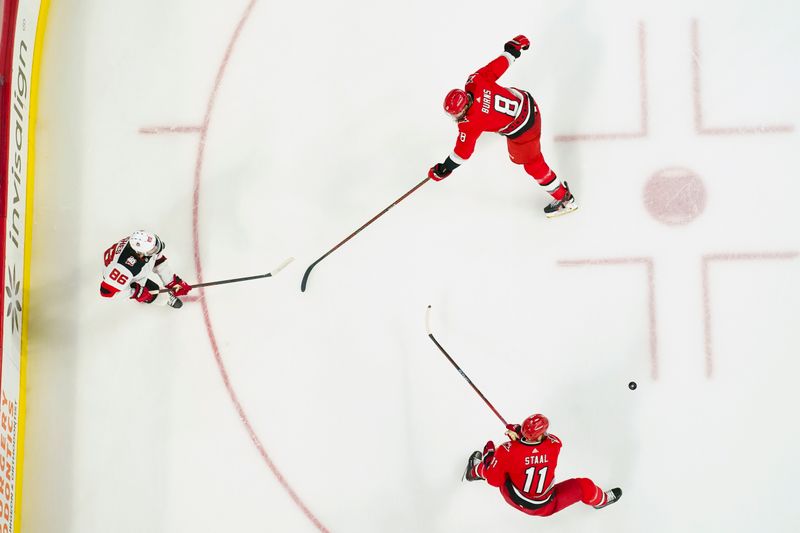 May 11, 2023; Raleigh, North Carolina, USA; New Jersey Devils center Jack Hughes (86) passes against Carolina Hurricanes defenseman Brent Burns (8) and center Jordan Staal (11) during the second period in game five of the second round of the 2023 Stanley Cup Playoffs at PNC Arena. Mandatory Credit: James Guillory-USA TODAY Sports