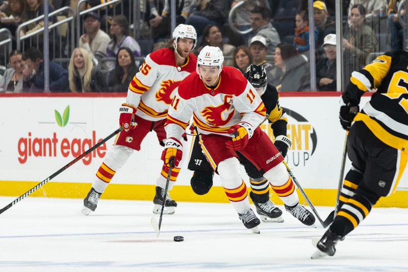 Oct 14, 2023; Pittsburgh, Pennsylvania, USA; Calgary Flames center Mikael Backlund (11) skates the puck away from Pittsburgh Penguins defenseman Erik Karlsson (65) during the second period at PPG Paints Arena. Mandatory Credit: Scott Galvin-USA TODAY Sports