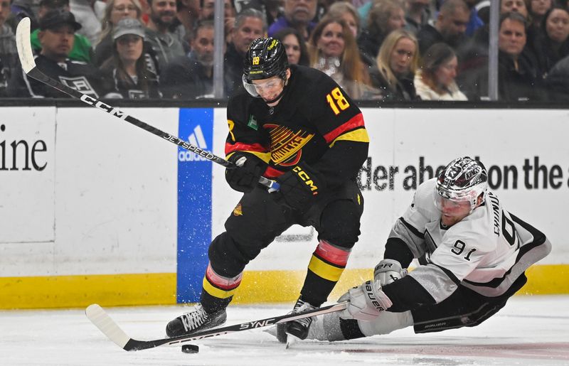 Apr 10, 2023; Los Angeles, California, USA;  Los Angeles Kings right wing Carl Grundstrom (91) reaches for the puck against Vancouver Canucks center Jack Studnicka (18) in the first period at Crypto.com Arena. Mandatory Credit: Jayne Kamin-Oncea-USA TODAY Sports