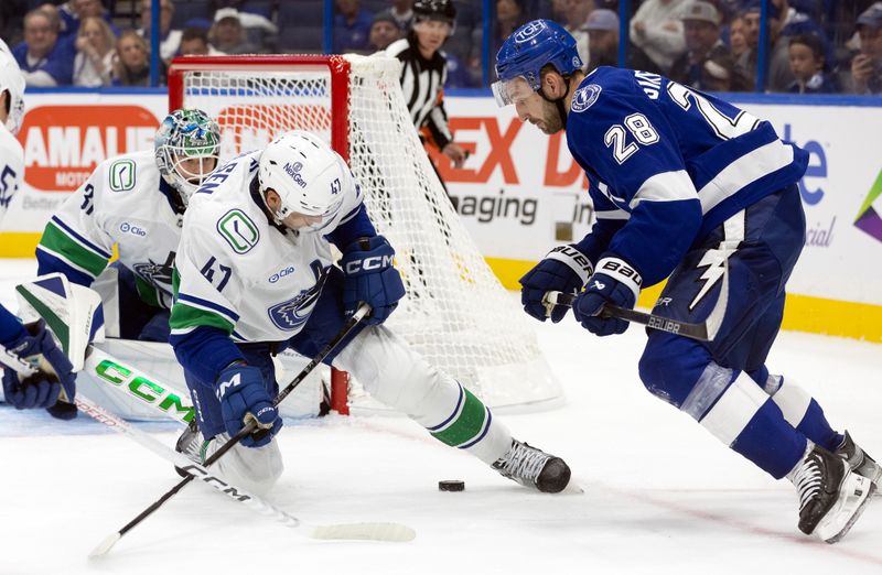 Oct 15, 2024; Tampa, Florida, USA; Tampa Bay Lightning center Zemgus Girgensons (28) and Vancouver Canucks defenseman Noah Juulsen (47) fight to defend the puck during the first period at Amalie Arena. Mandatory Credit: Kim Klement Neitzel-Imagn Images