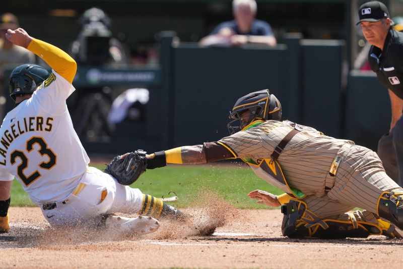 Apr 9, 2025; West Sacramento, California, USA; Athletics catcher Shea Langeliers (23) scores a run as San Diego Padres catcher Martín Maldonado (center) applies a tag during the second inning at Sutter Health Park. Langeliers was originally called out but the call was overturned after a video review.  Mandatory Credit: Darren Yamashita-Imagn Images